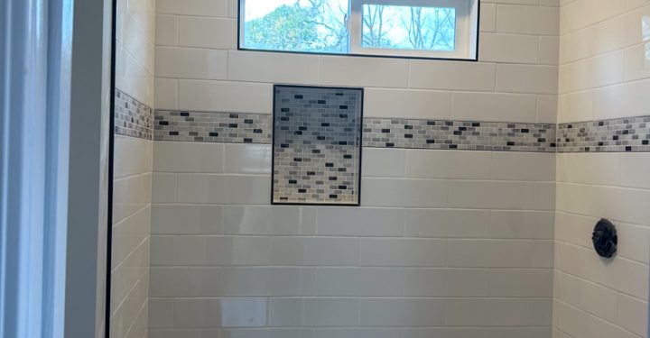 A bathroom remodeled, with upgraded tile backsplash, a shower niche, and fixtures yet to be installed.